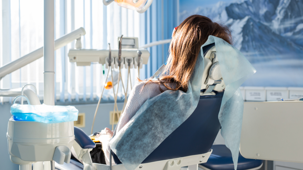 A woman is sitting in a dental chair in a dental office.