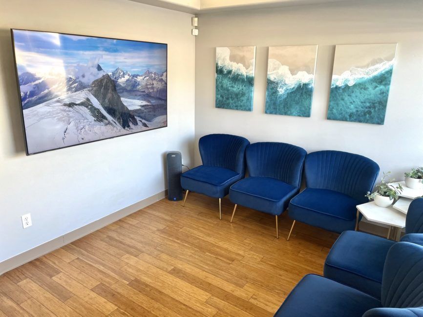 A waiting room with blue chairs and a flat screen tv on the wall.