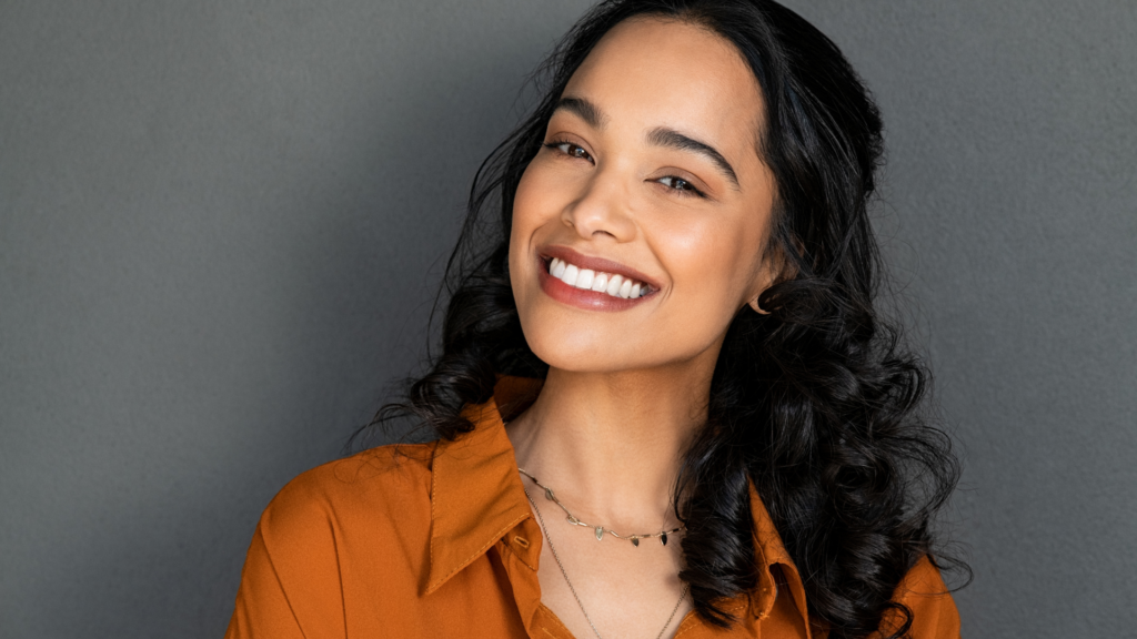 A woman with curly hair is smiling and wearing a necklace.