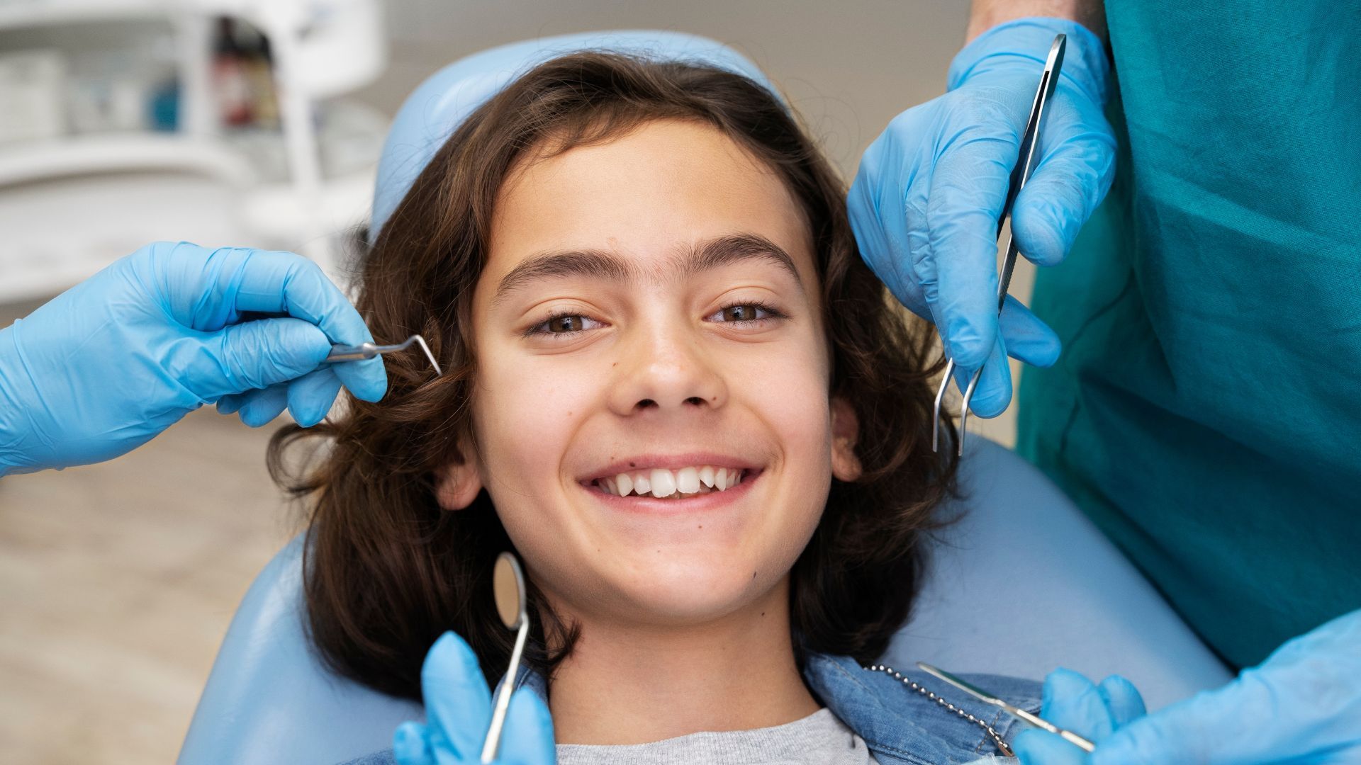 Smiling child in a dental chair as blue-gloved dentists work nearby