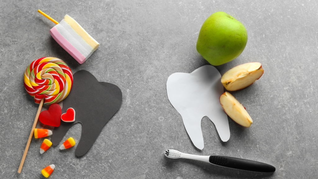 A tooth made out of paper , an apple , candy corn , lollipops and a toothbrush on a table.