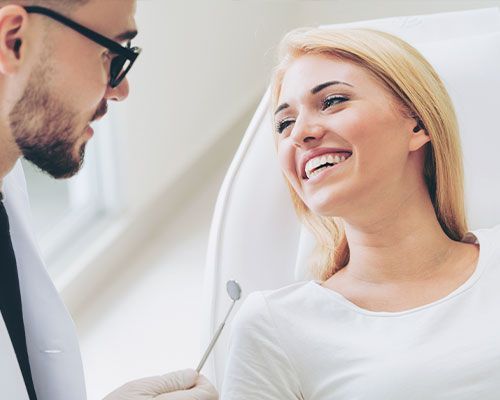 A woman is smiling while having her teeth examined by a dentist.