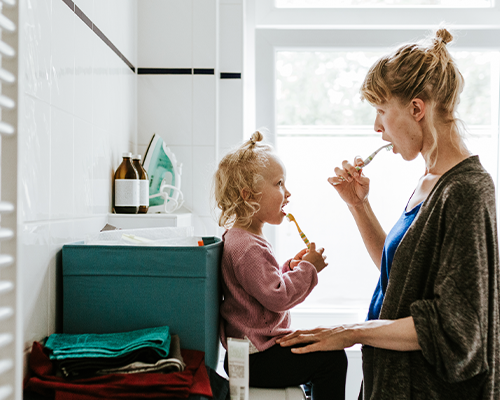 A woman is brushing her daughter 's teeth in the bathroom.