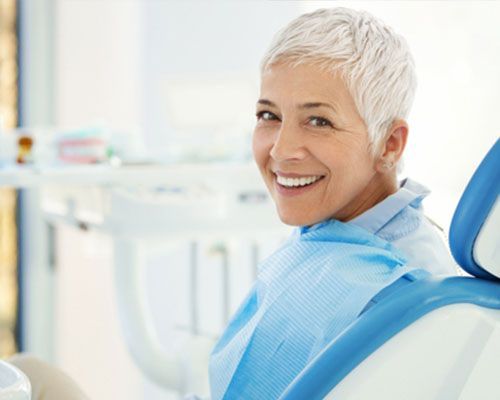 A woman is smiling while sitting in a dental chair.