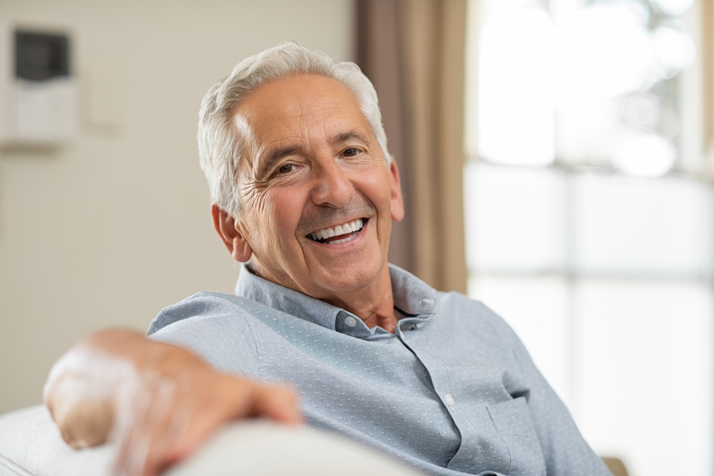 Smiling man in a light blue shirt sitting on a couch in a bright living room
