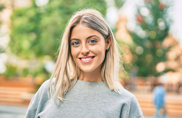 A young blonde woman wearing a grey sweater is smiling and looking at the camera.