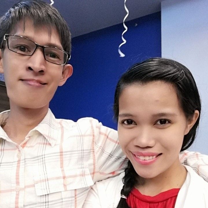 Two people smiling; one in glasses, plaid shirt; one with braided hair, white jacket, red shirt.