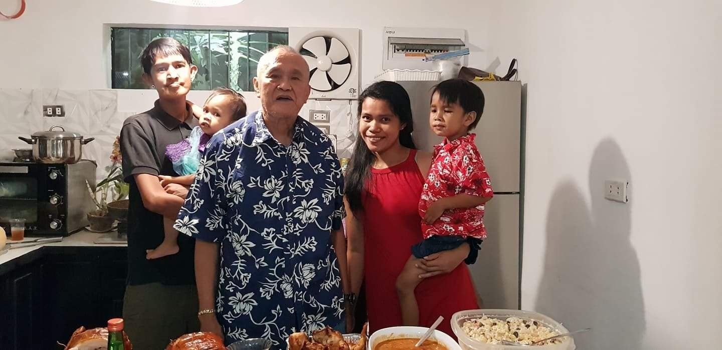 Family gathering in a kitchen; smiling people, holding babies, food on the counter.