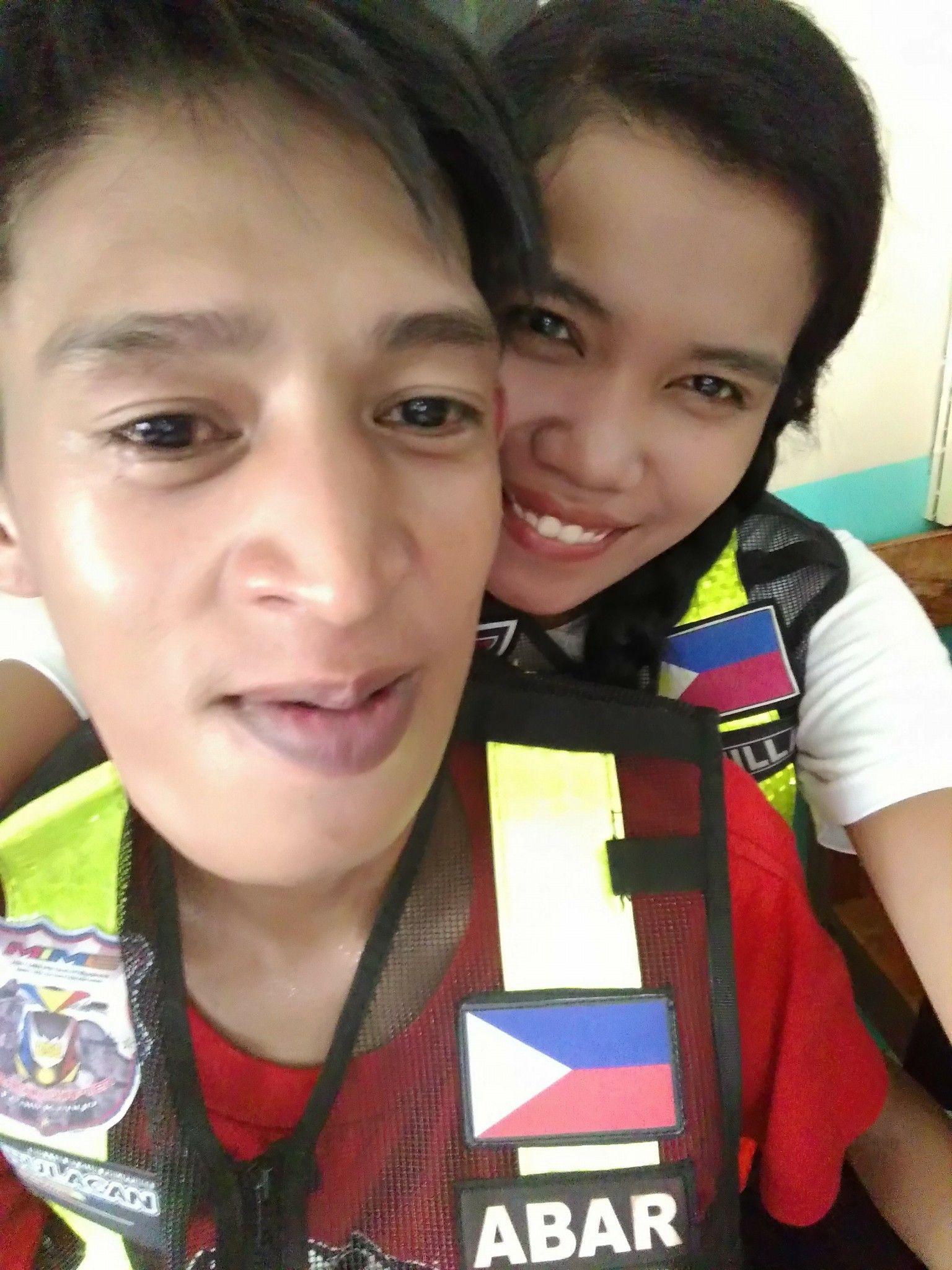 Two people, smiling, wearing vests with Philippine flag patches.
