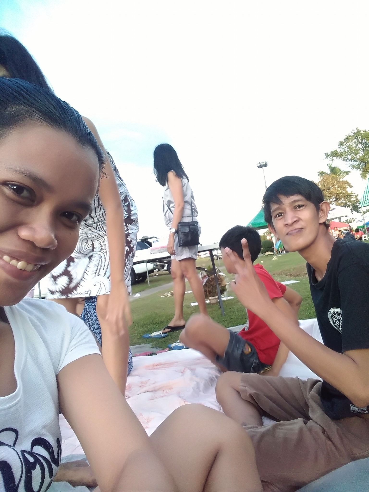 People on a blanket, one woman smiling, other people in the background, outdoors.