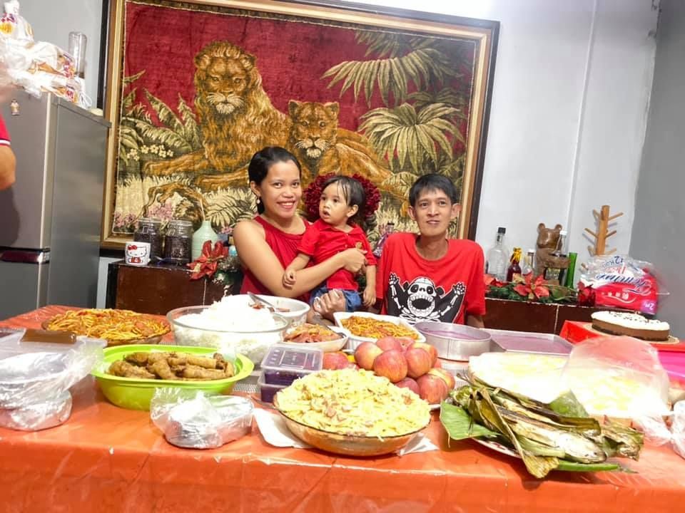 Family smiling behind a table of food. A tapestry of lions hangs on the wall.
