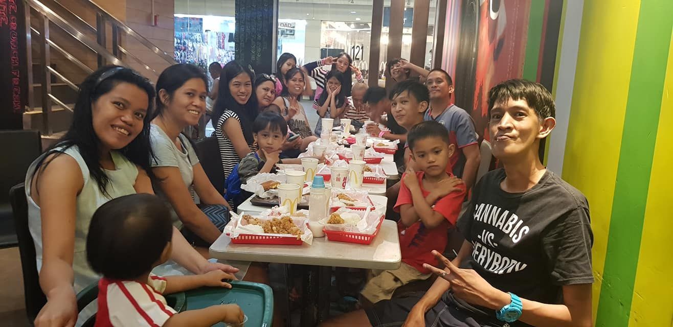Group of people eating at a restaurant table. Many fried chicken boxes on the table. They smile.