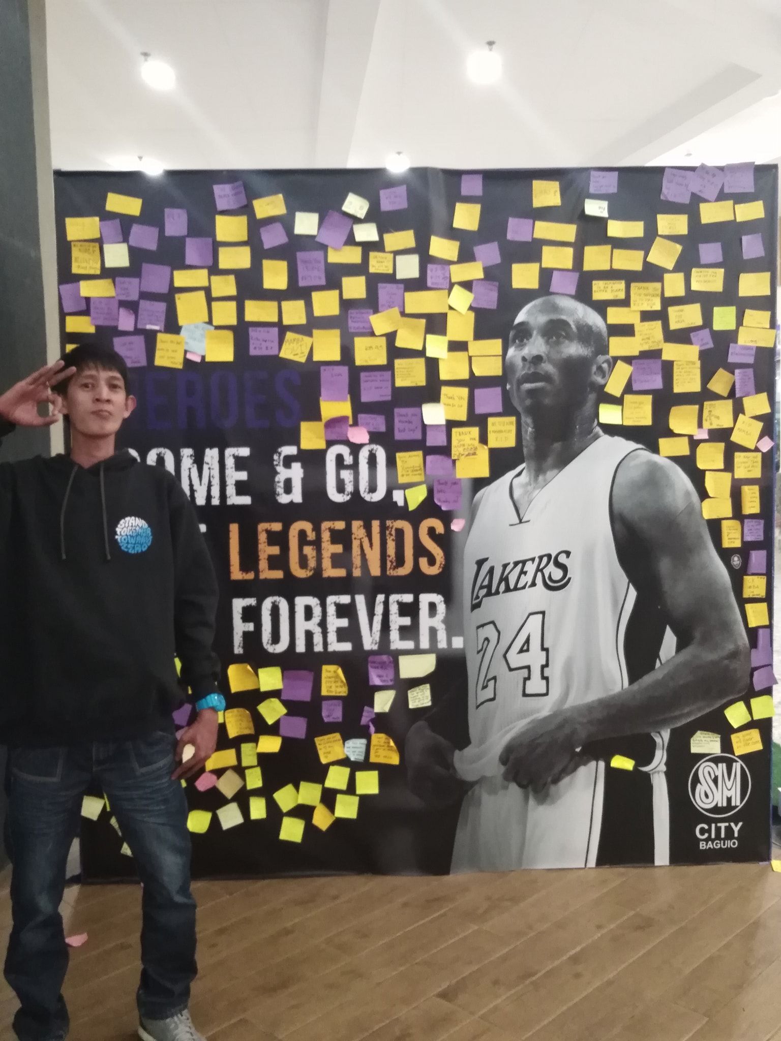 Man salutes next to Kobe Bryant memorial with sticky notes at SM City.