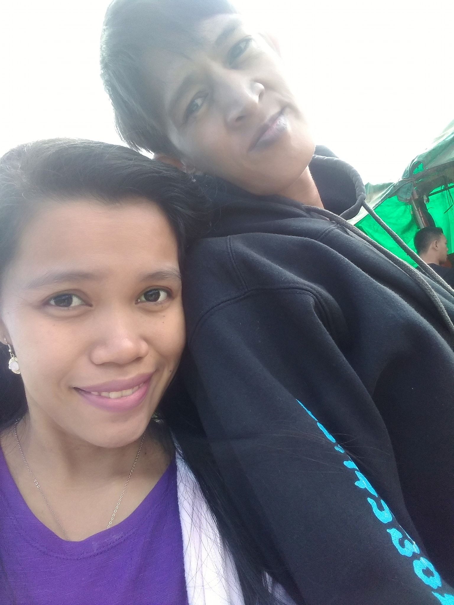 Woman and person in black hoodie, heads close together, smiling, selfie.