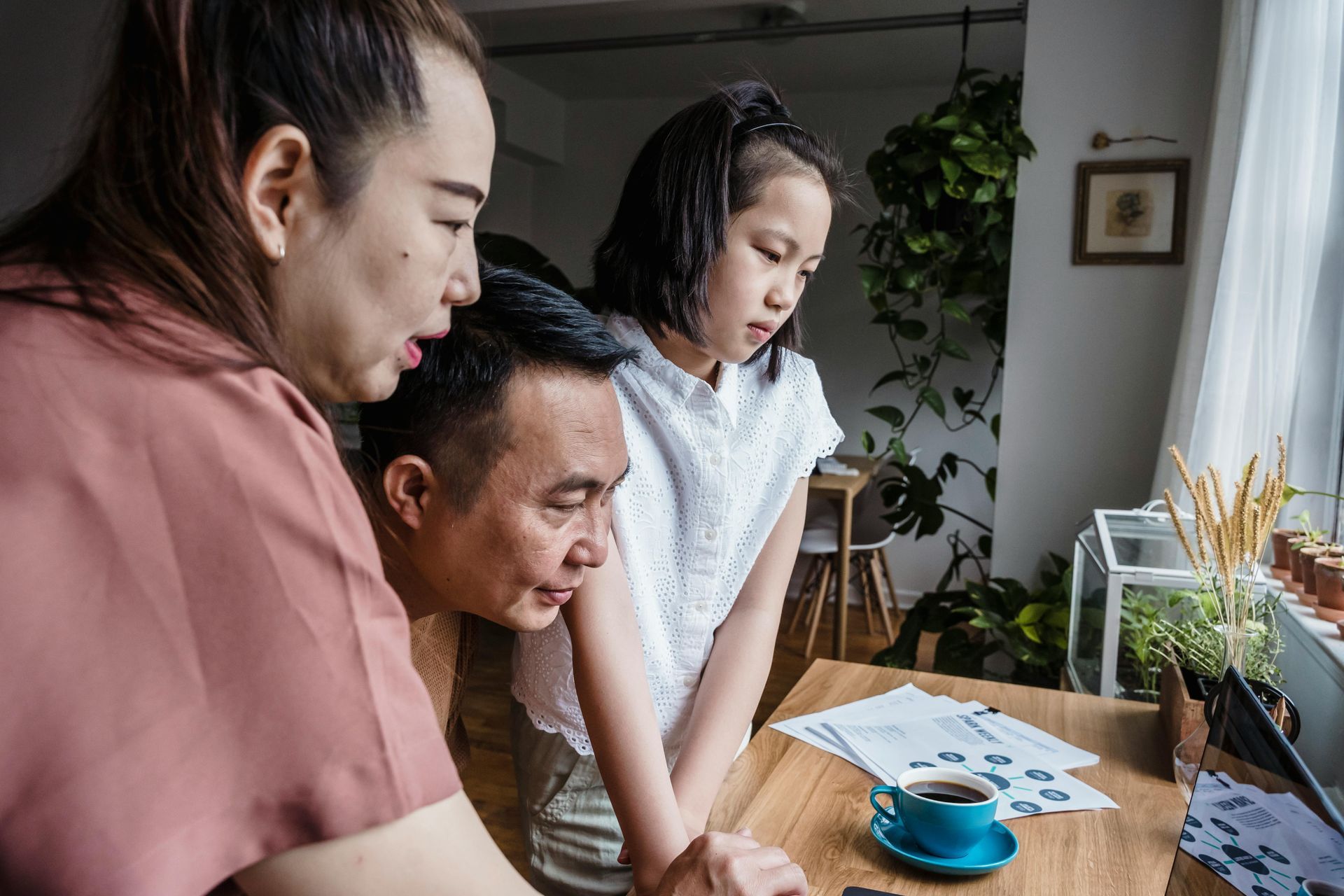 Family looking at a laptop screen together, papers and coffee on the table.
