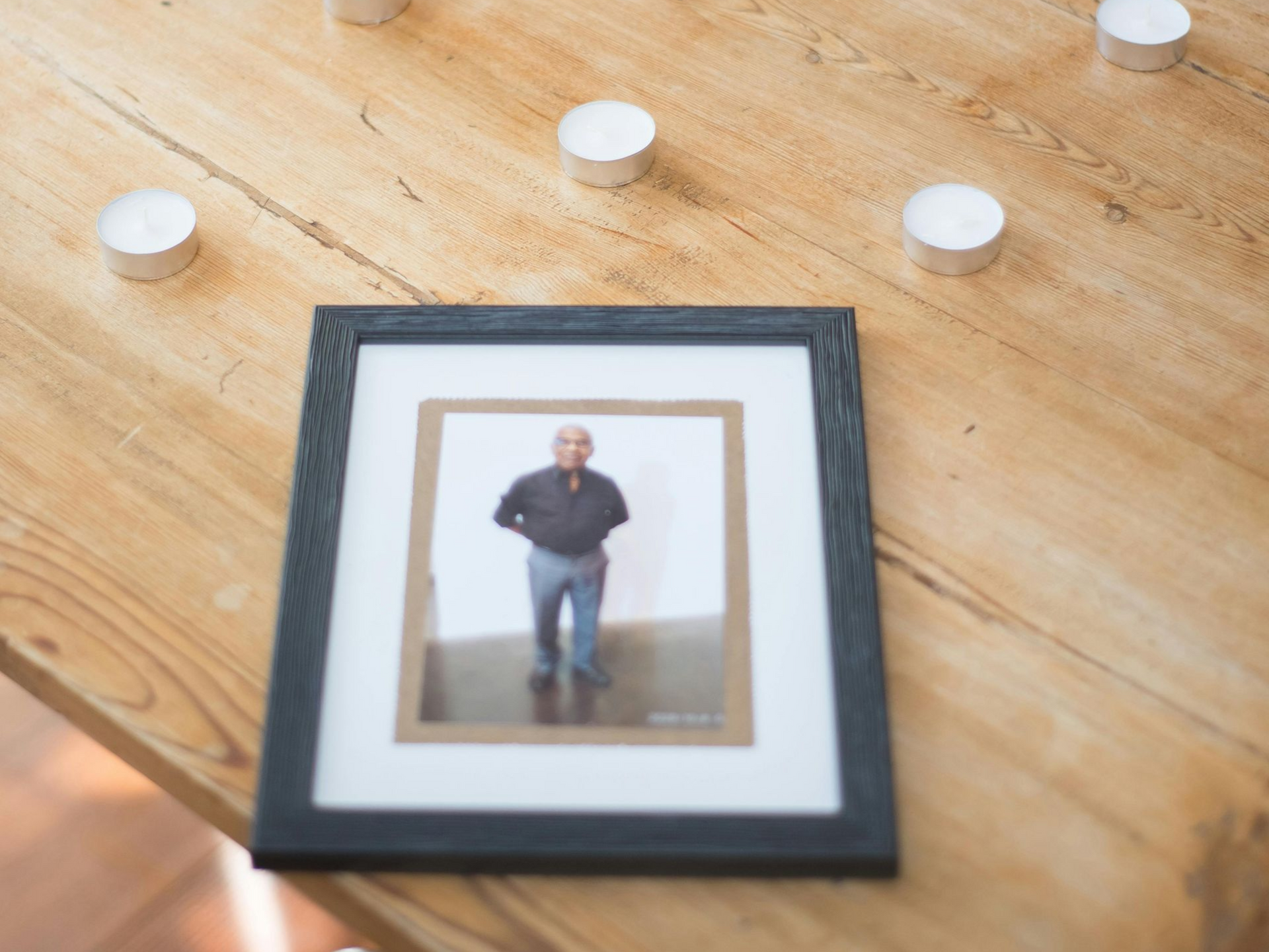 Photograph of a man in a frame on a wooden table, surrounded by tea light candles.
