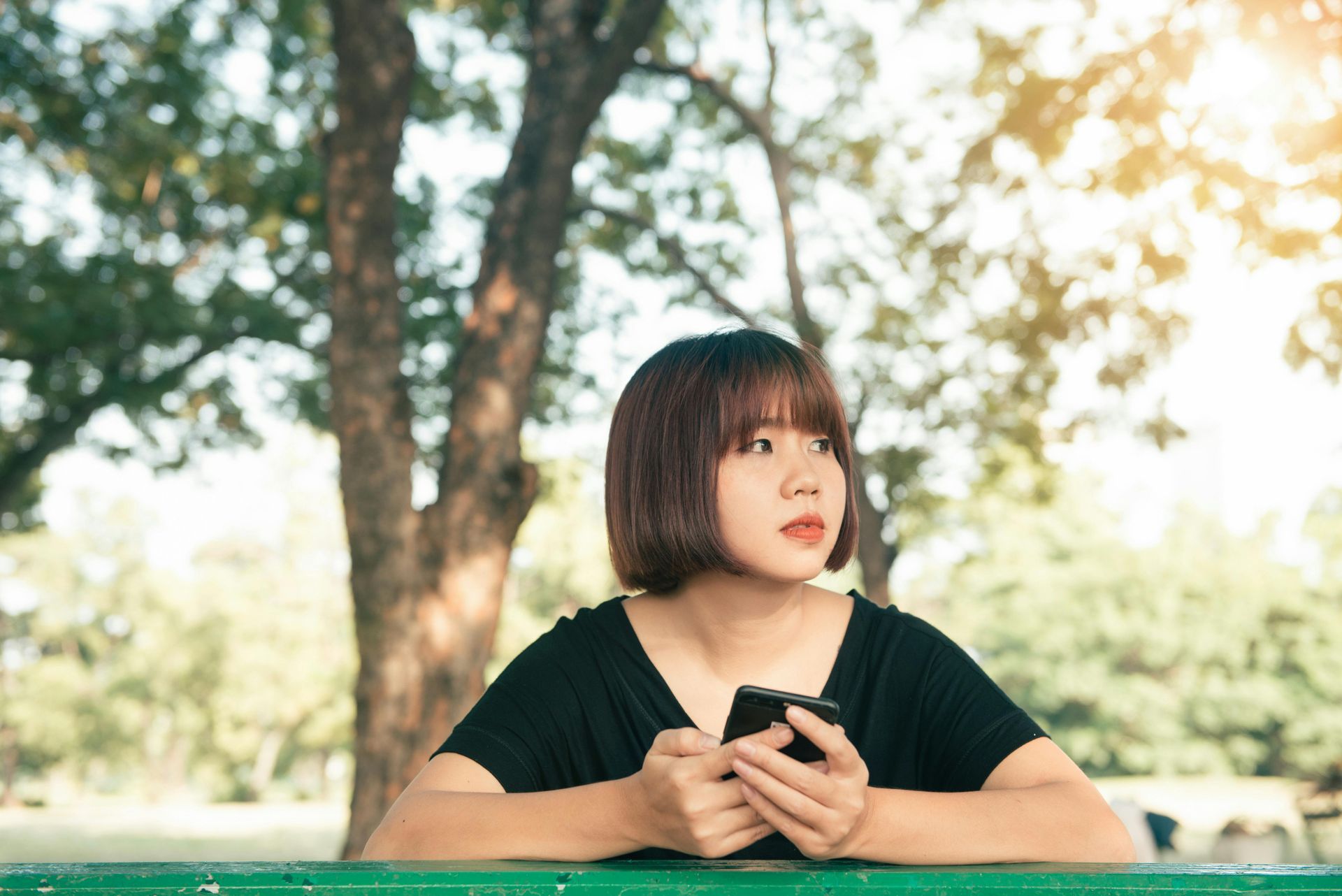 Woman with short hair, holding a phone, looking off to the side, outdoors.