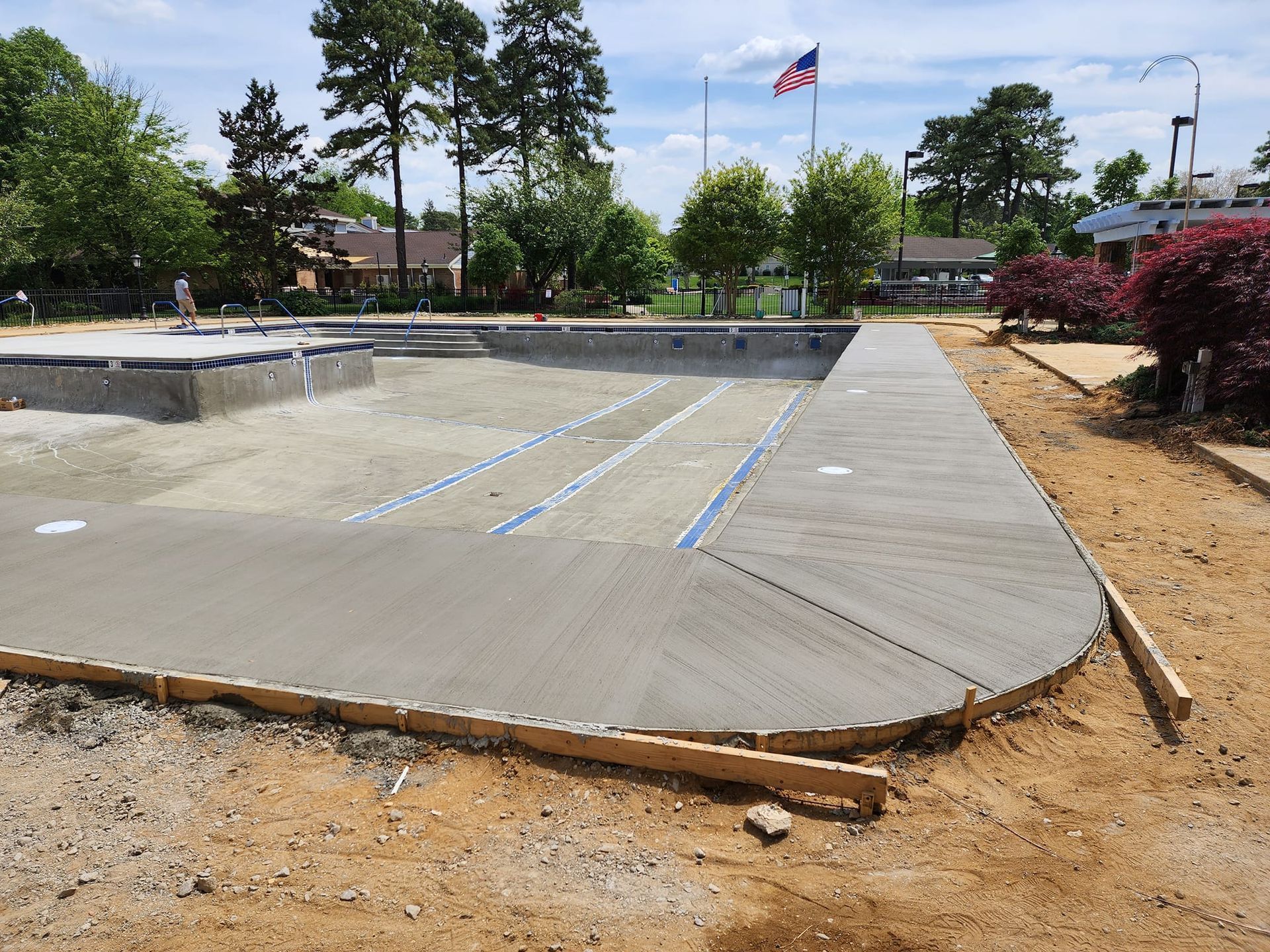 Construction site: New pool with concrete decking, surrounded by dirt and landscaping. American flag in the background.