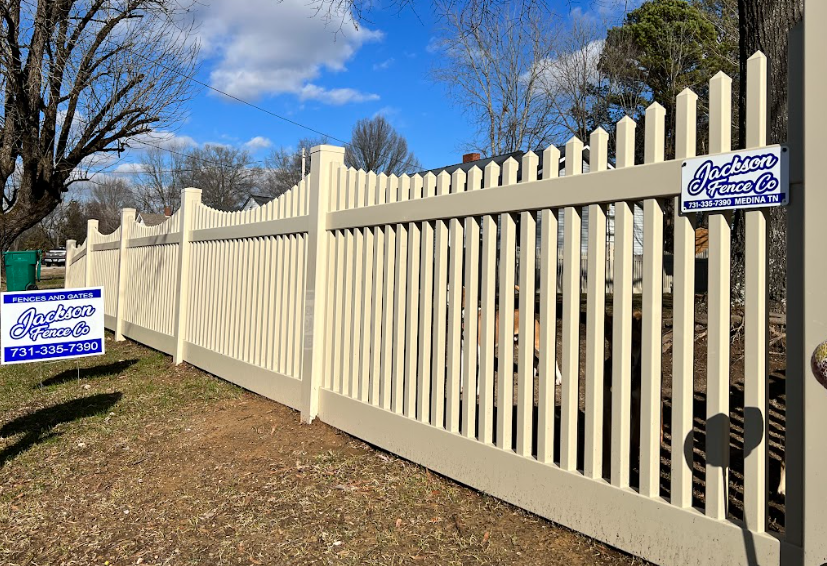 A close up of a white vinyl fence with trees in the background.