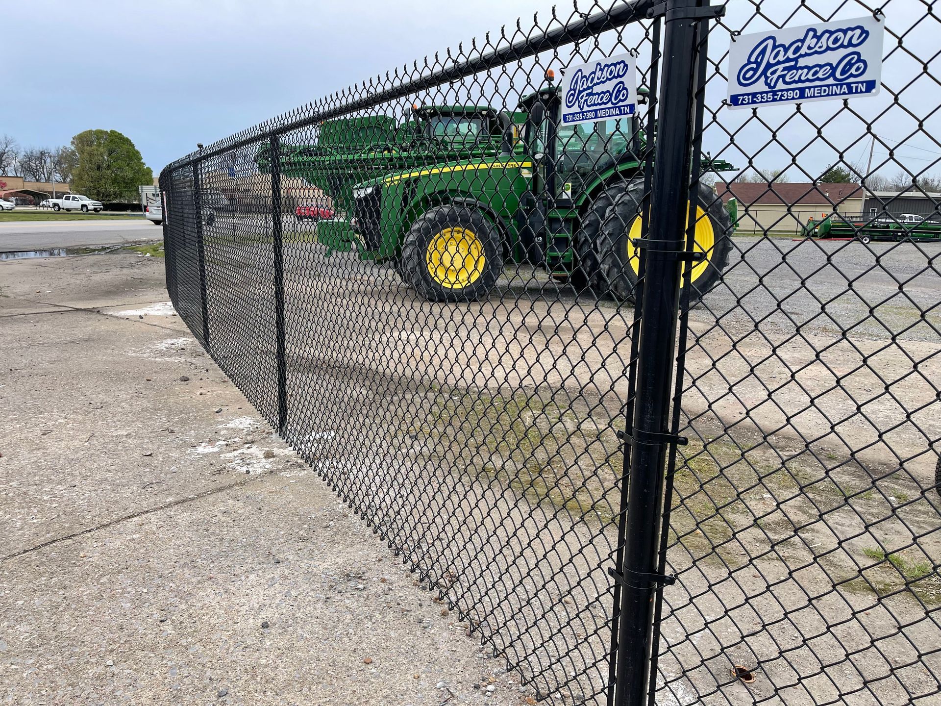 Black chain-link fence in front of a green tractor with yellow wheels. 