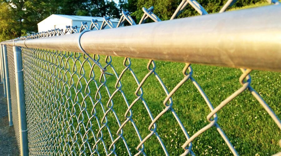 A concrete pathway stretches between two black chain-link fences under a clear blue sky, viewed from a dirt-covered foreground.