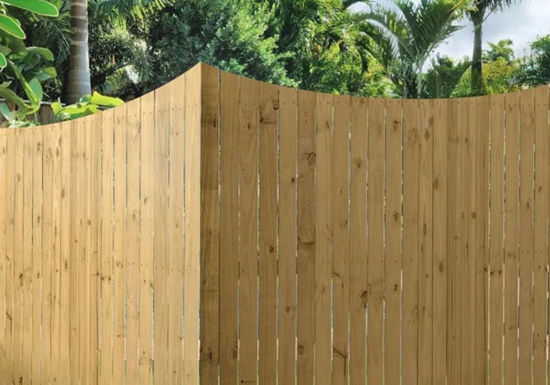 A wooden fence with a curved corner is surrounded by trees.