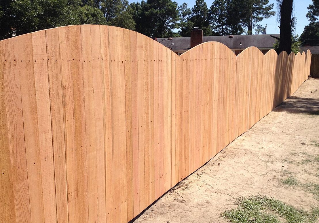 A wooden fence with a curved top is in a yard.