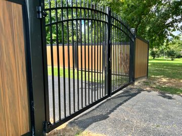 A wrought iron gate with a wooden fence behind it.