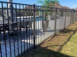 A metal fence surrounds a patio with tables and chairs and a pool.