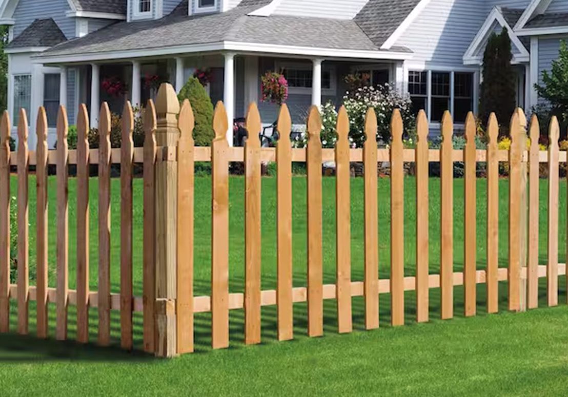 A wooden picket fence surrounds a lush green lawn in front of a house.