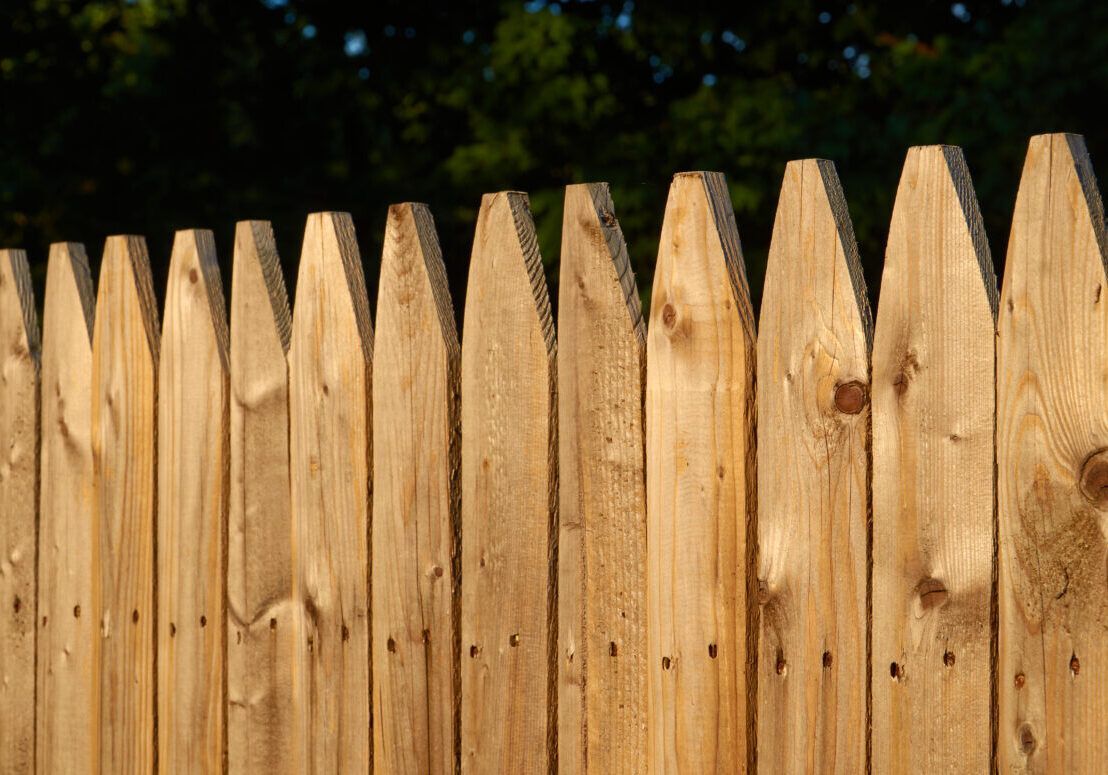 A close up of a wooden picket fence with trees in the background.