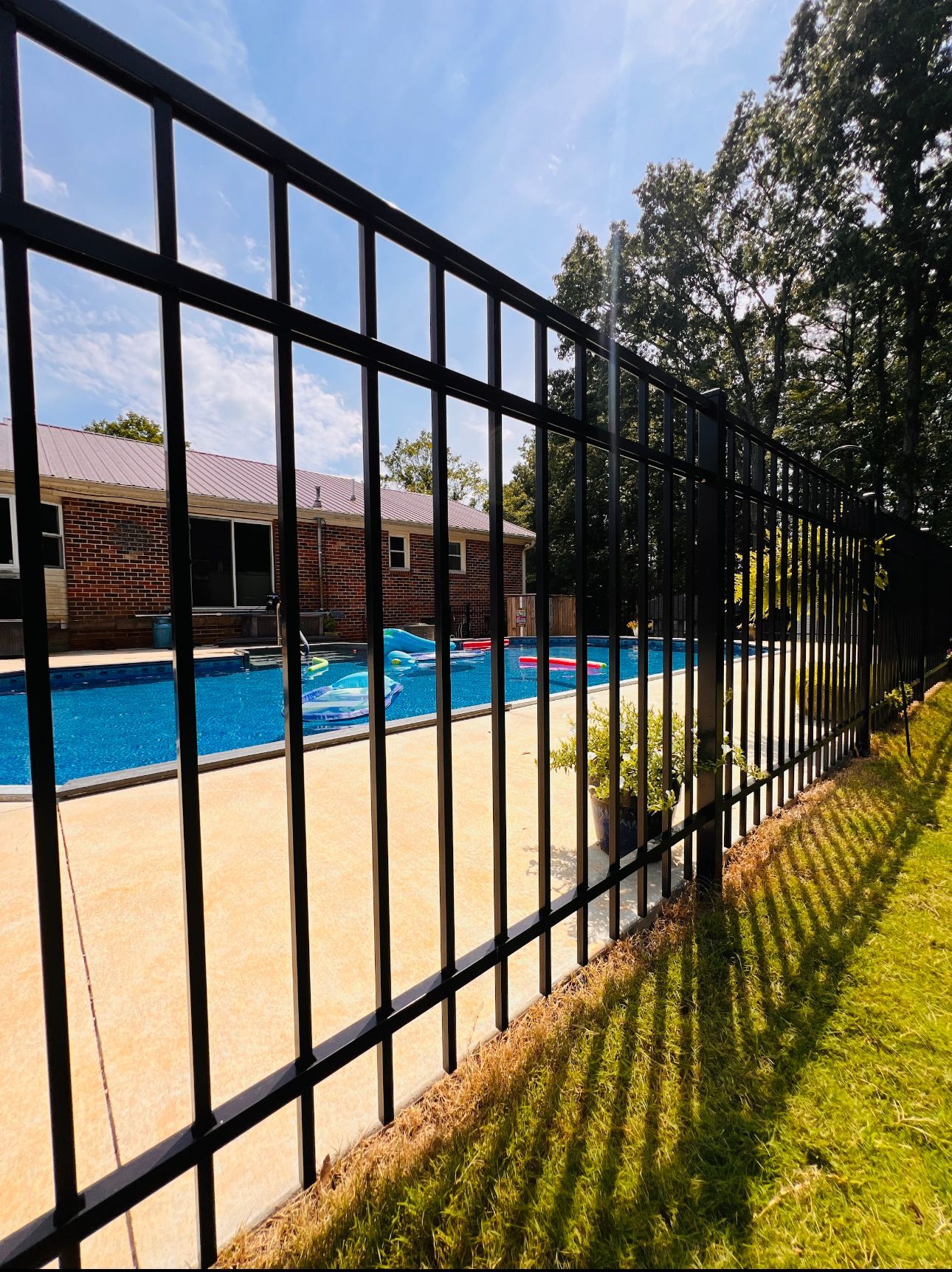 A black metal fence surrounds a swimming pool with a house in the background.