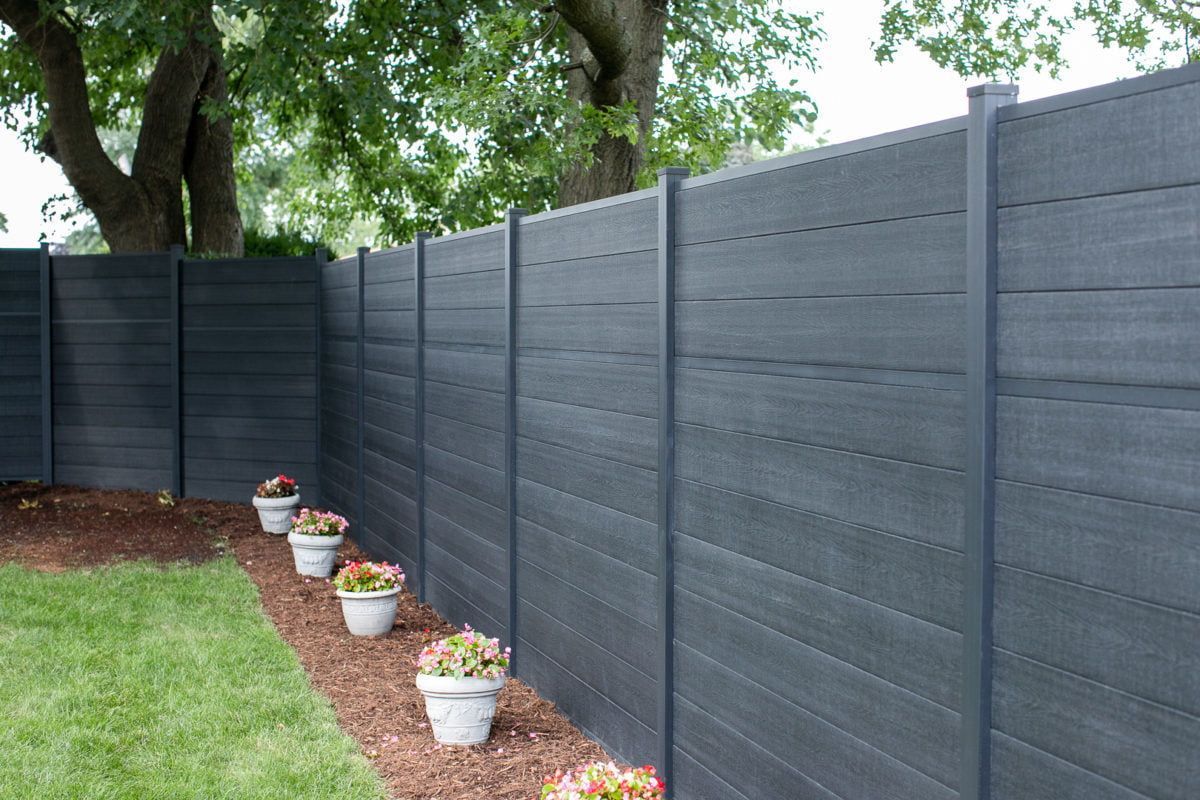 Dark gray privacy fence in a backyard garden with potted flowers.