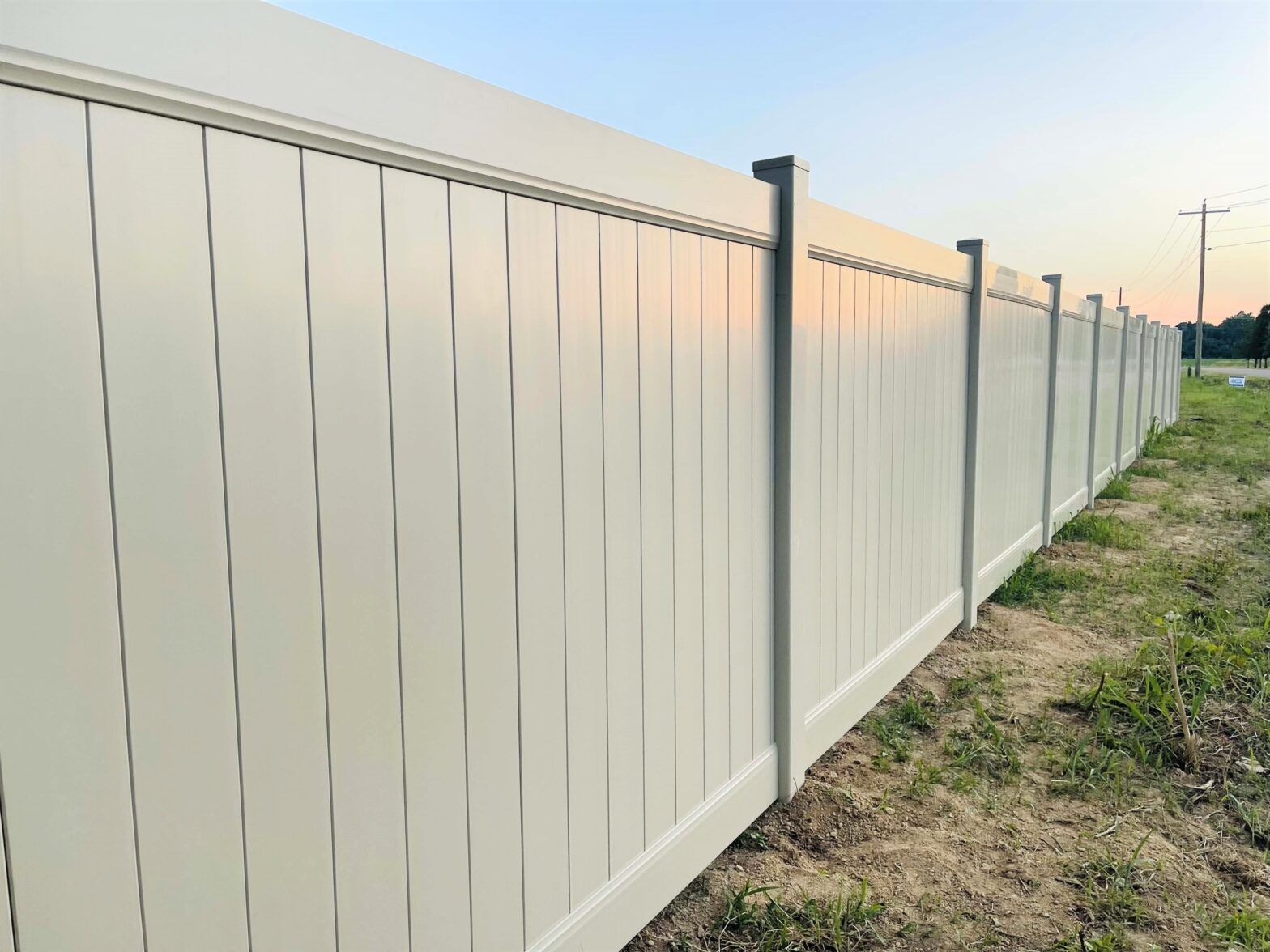 A white vinyl fence is sitting in the middle of a grassy field.