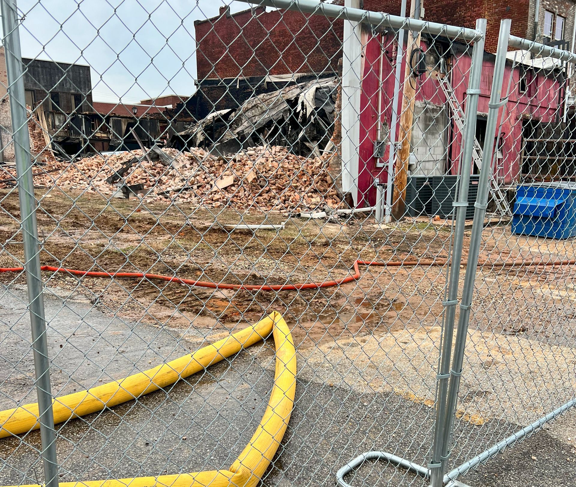 A chain link fence with a yellow hose in front of it.