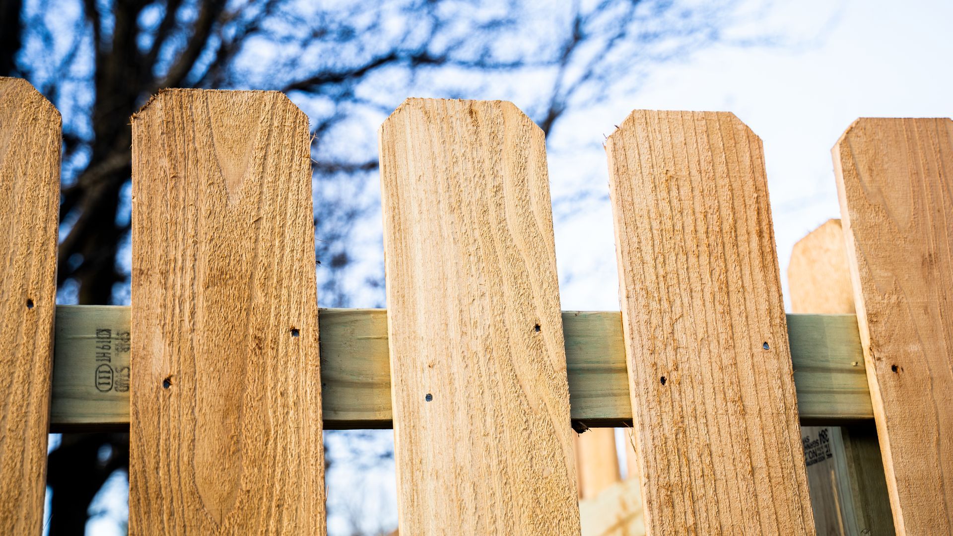 A close up of a wooden picket fence with trees in the background.