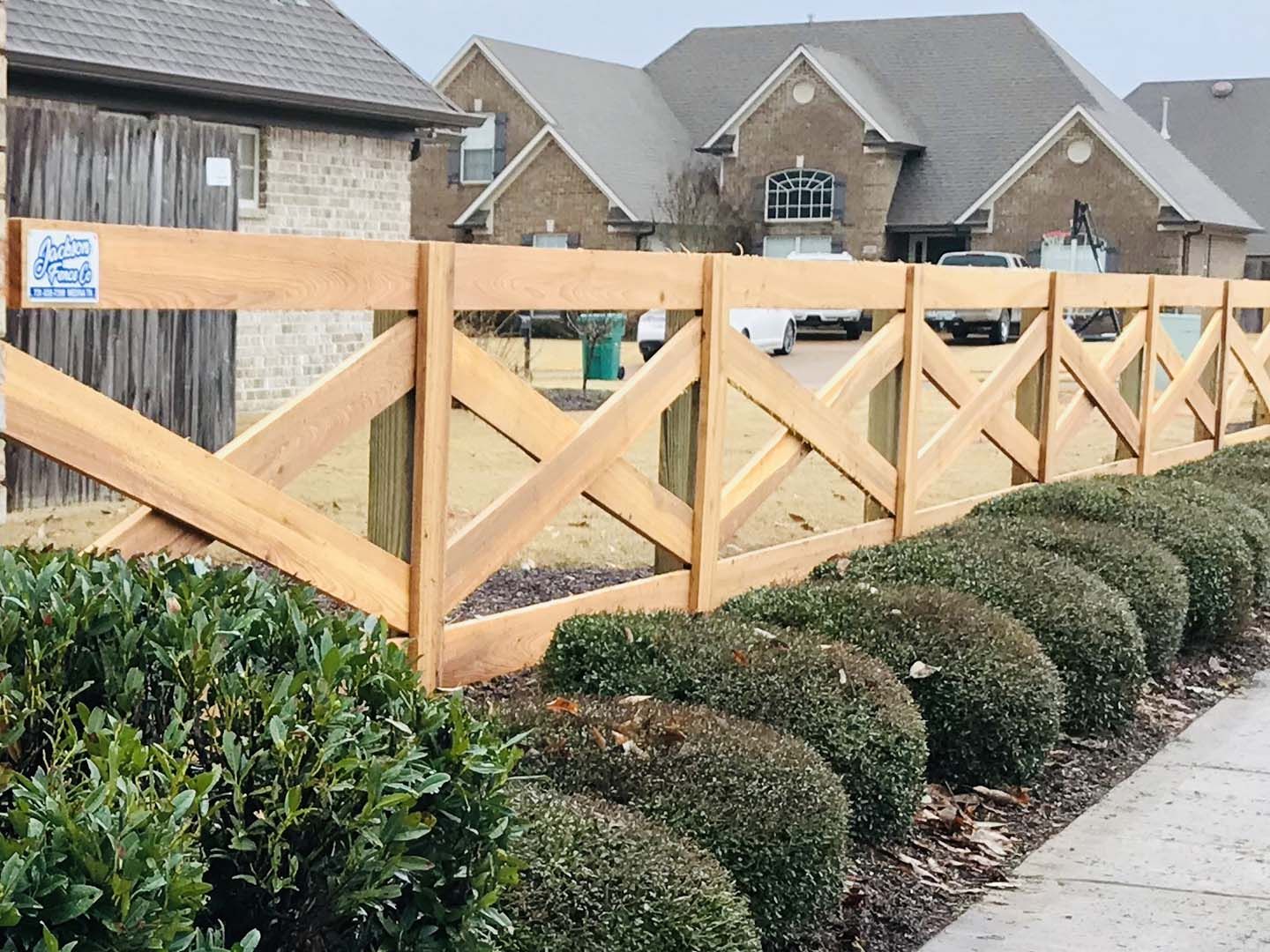 A wooden fence is surrounded by bushes and houses in a residential area.
