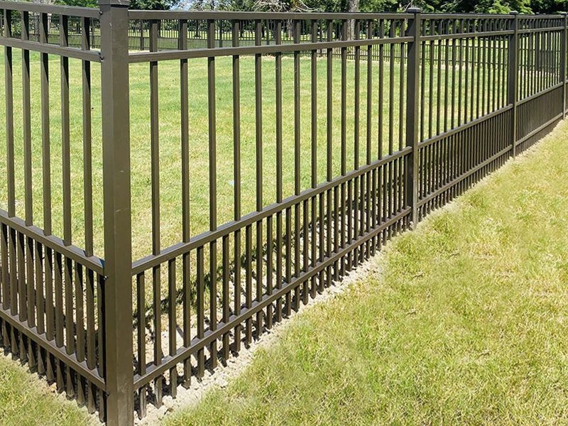 A metal fence is surrounding a lush green field.