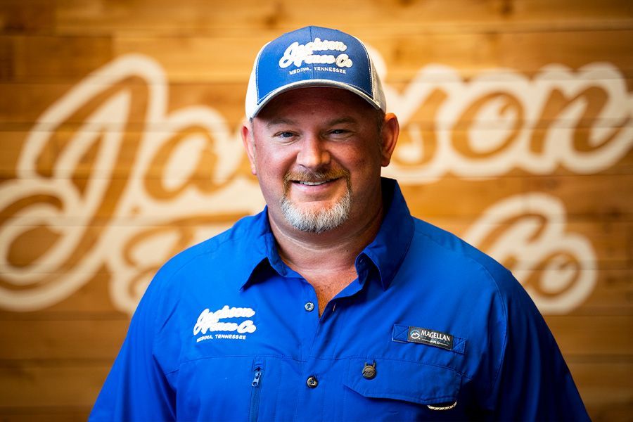 A man in a blue shirt and hat is standing in front of a wooden wall.