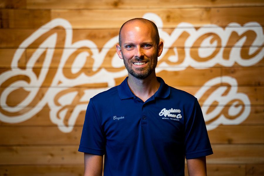 A man in a blue shirt is standing in front of a wooden wall.