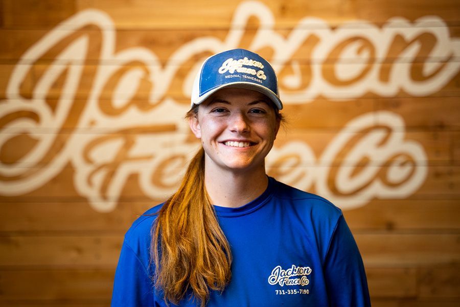 A woman wearing a blue hat and a blue shirt is smiling in front of a wooden wall.