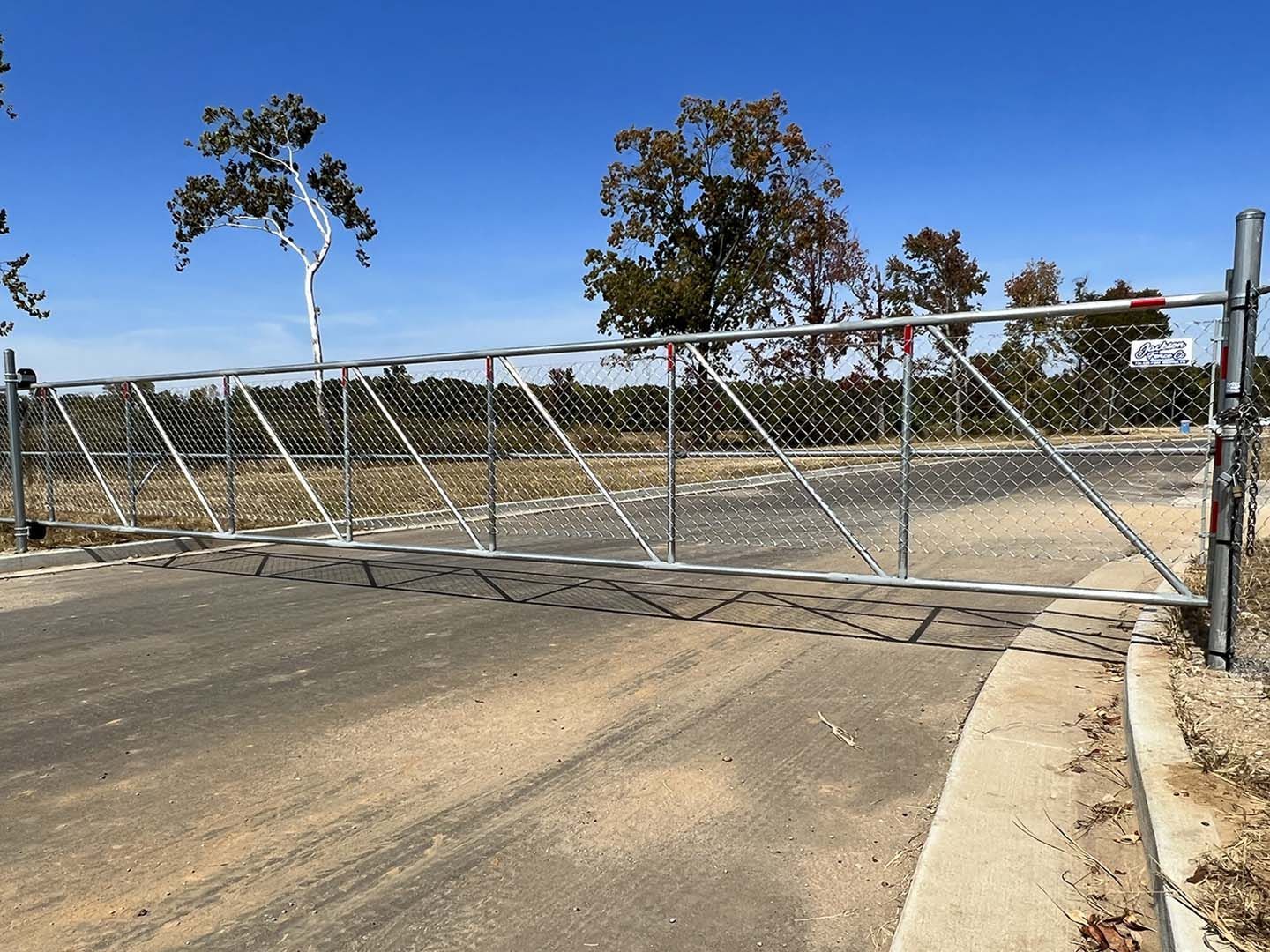A chain link fence blocking a road with trees in the background