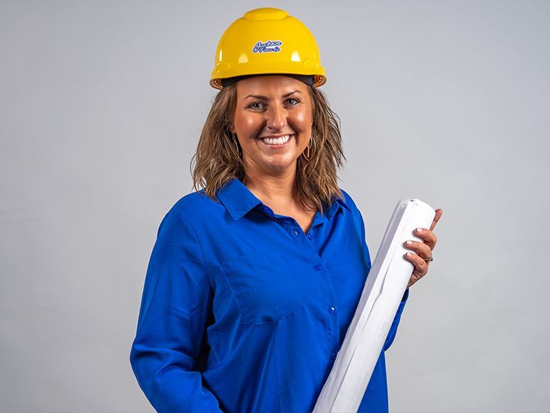 A woman wearing a hard hat and a blue shirt is holding a roll of blueprints.