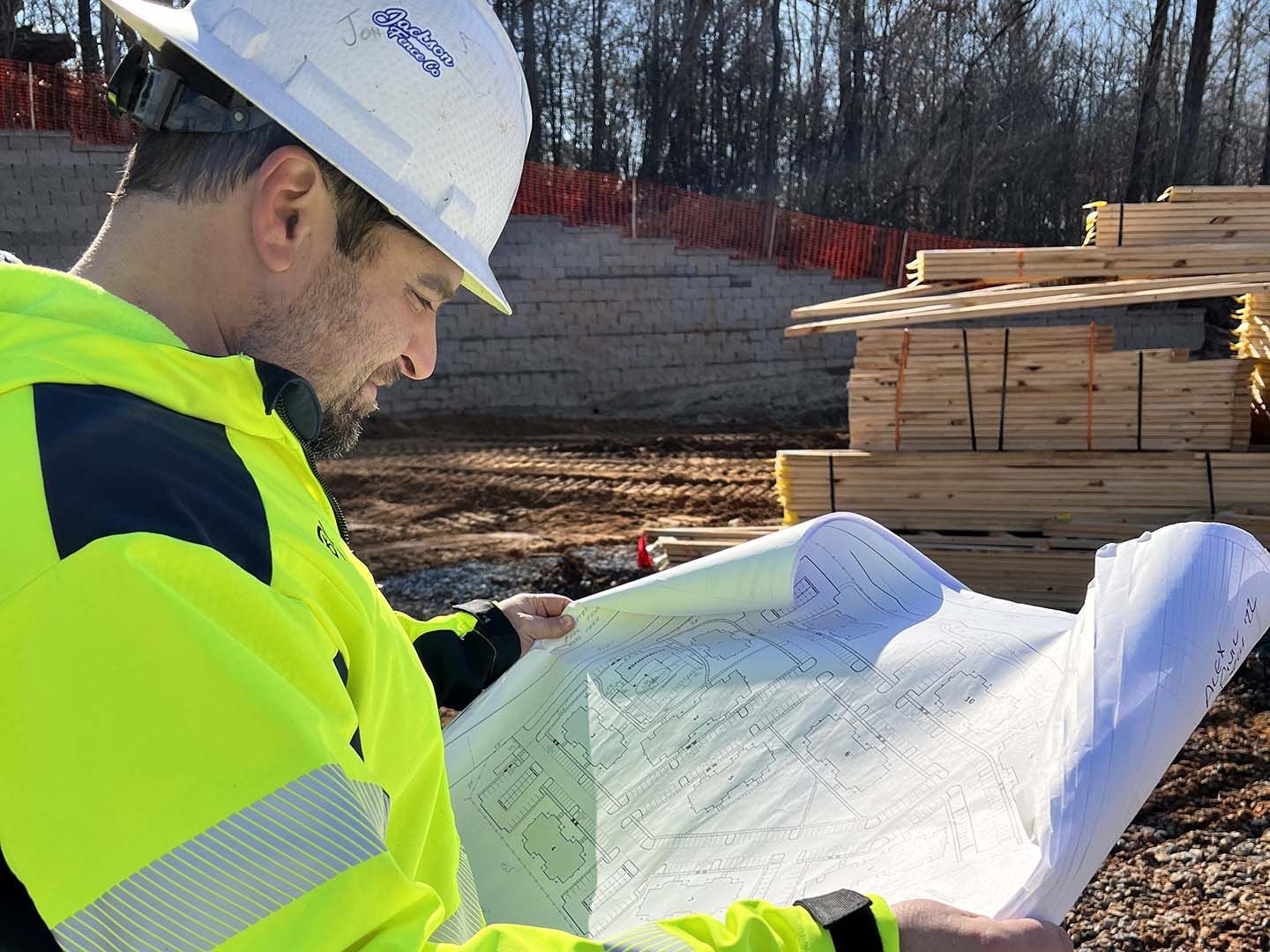 A man wearing a hard hat and safety vest is looking at a blueprint.