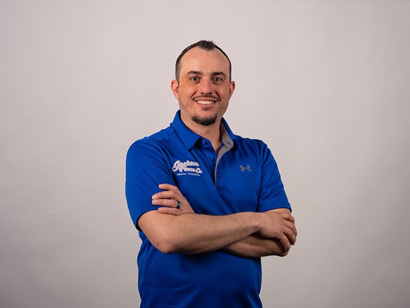 A man in a blue shirt is standing with his arms crossed and smiling.