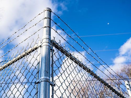 A chain link fence with barbed wire against a blue sky.