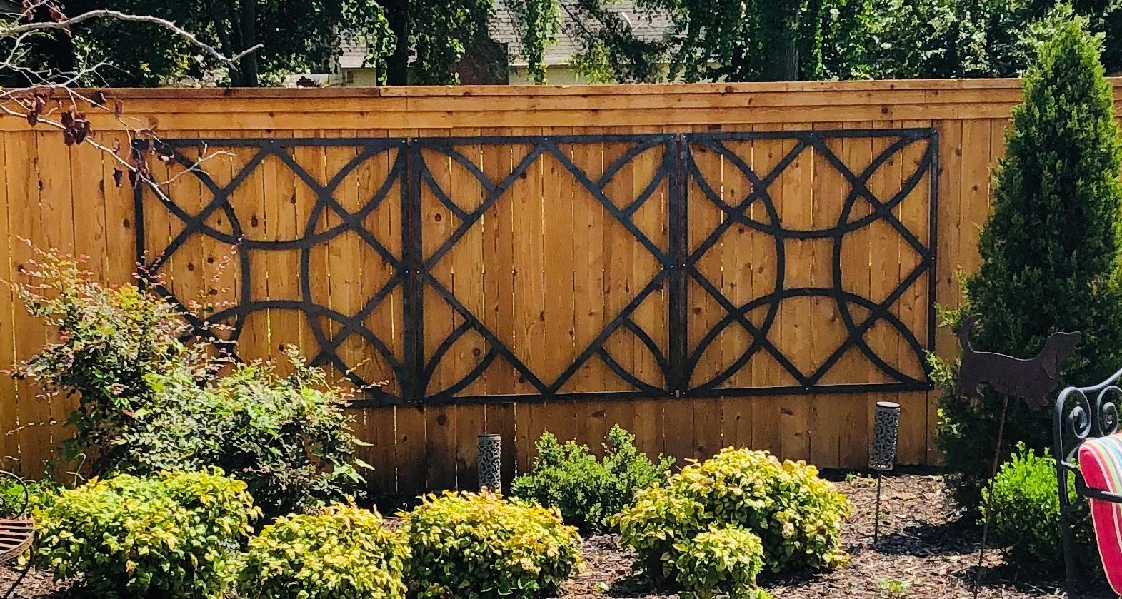 Wooden fence with decorative metalwork. Green shrubs in front.