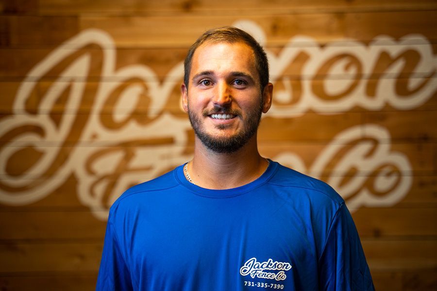 A man in a blue shirt is standing in front of a wooden wall.