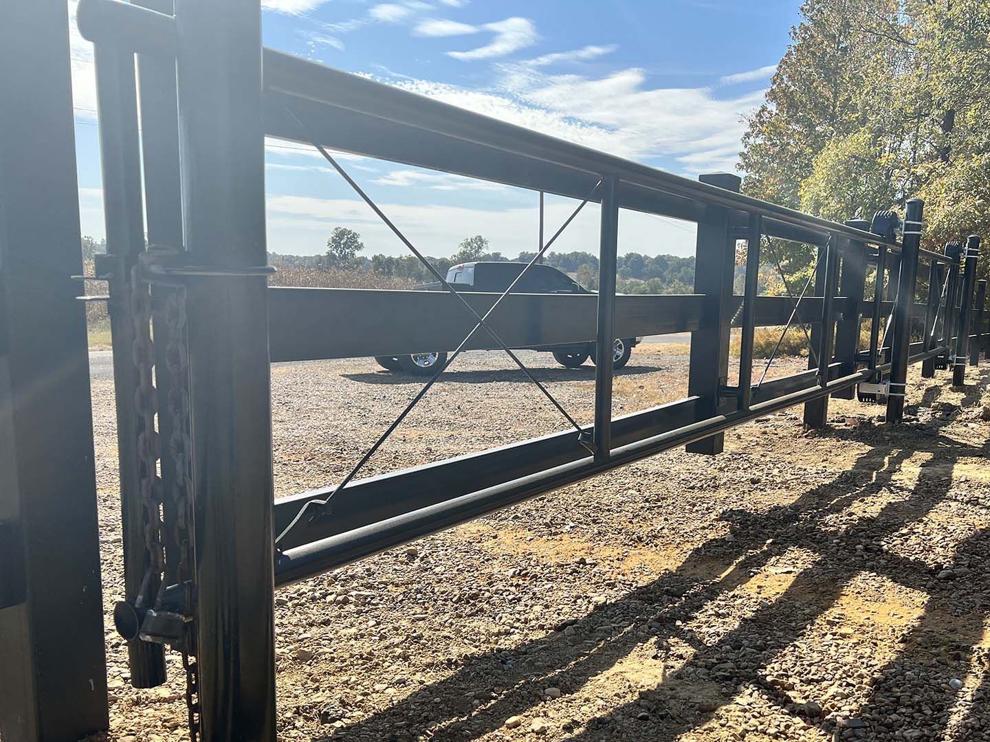 A truck is parked in a gravel lot behind a metal fence.