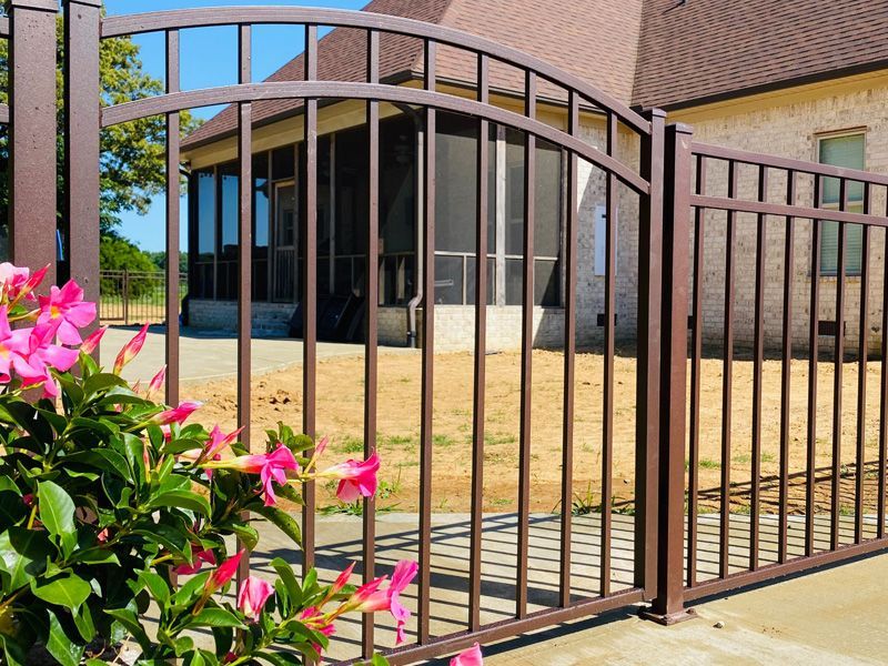 A fence with flowers in front of it and a house in the background